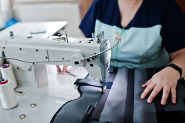 Female hands stitching fabric on professional manufacturing machine at workplace. Sewing process.