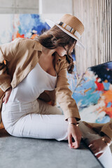 a beautiful girl with long hair in a jacket and a sand-colored hat and white trousers and a T-shirt advertises clothes