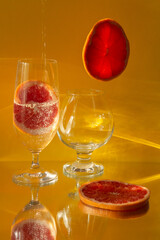 A closeup shot of grapefruit slices and glasses of water on a specular surface against a yellow background