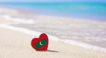 Fototapeta na wymiar Flag of the Maldives in the shape of a heart on a sandy beach. The concept of the best vacation in Maldives resorts