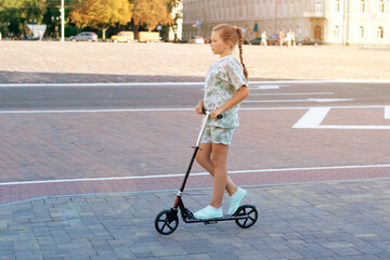 Cute teen girl rides around town on a scooter sunny summer day.