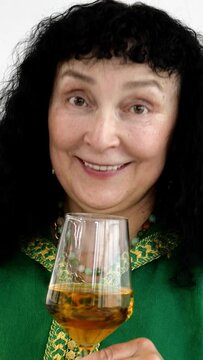 Portrait of brunette woman mature adult, caucasian ethnicity or mixed race, drinking wine enjoying in public place and says toast. Focus on foreground. Vertical video. Close-up.