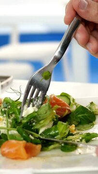 Caucasian ethnicity human hands holding fork and knife, cut herbs in tasty fresh salad. Salad with salmon, avocado, tofu cheese and spinach. Healthy vegetarian food. Vertical video.