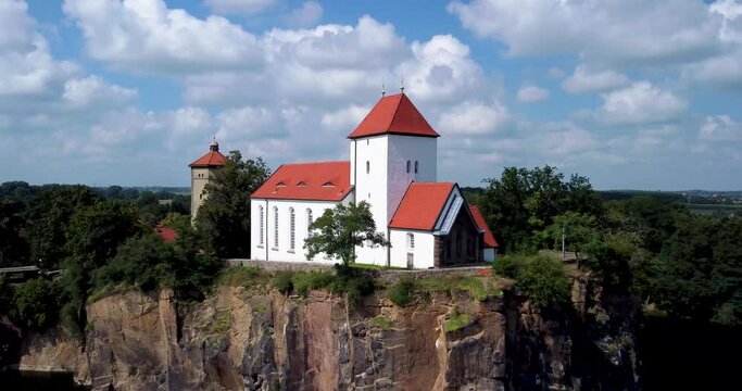 Church (13th century, 1848) on a mountain spur, surrounded by a lake or flooded quarry. Aerial view footage.