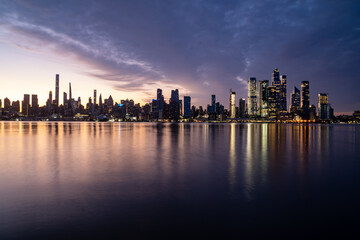 Obraz premium New York, NY - USA - Horizontal image of the skyline of the westside of Manhattan at sunrise, with reflections seen in the Hudson River.