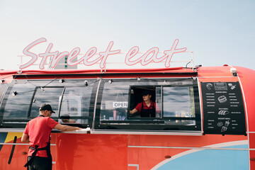 Two young workers in uniform cleaning red food truck in the beginning of working day