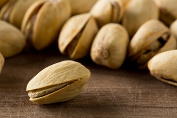Close up of single pistachio in front of heap of salted, roasted green pistachio nuts snack over wooden background, healthy food snack
