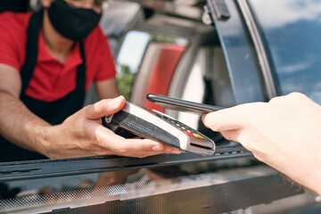 Seller of takeout food holding payment terminal in window of truck while client paying for snack