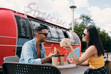 Happy young couple in sunglasses and casualwear having fast food and drinks by conversation in outdoor cafe - Powered by Adobe