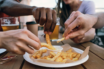 Hands of intercultural hungry friends putting french fries into sauce before eating - obrazy, fototapety, plakaty