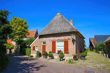 Fototapeta na wymiar view on typical old dutch stone house with thatched roof against blue summer sky in small rural village - Bronkhorst, Netherlands