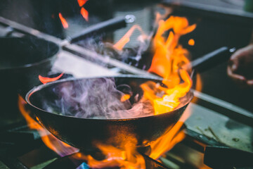 Chef cocinando con fuego en sartén.