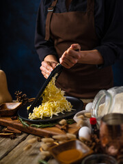 A chef grates a pumpkin to make a traditional American pumpkin pie. Many ingredients lie side by side on a wooden table. Thanksgiving, Halloween, Christmas, family holidays.