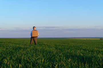 a businessman holds a cardboard box and poses on a green grass field - business concept