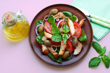 Italian Panzanella salad with bread, tomatoes, red onion, basil, capers and olive oil on pink background. Top view
