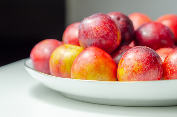 Closeup on fresh and ripe plums on a white ceramic plate