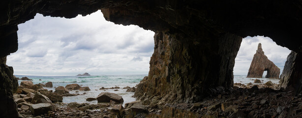 Playa de Campiechos, en Asturias. Cueva en una playa preciosa, con el mar al fondo y nubes. Piramide de piedra en el horizonte.