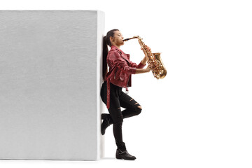 Full length profile shot of a young female saxophonist playing against a wall