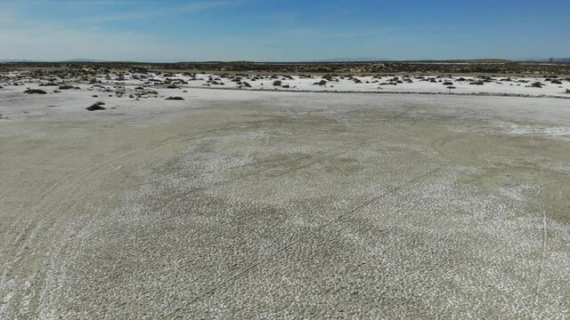 Rise up flight over bare salty playa marked with multiple vehicle tracks next to highway Fallon Nevada.