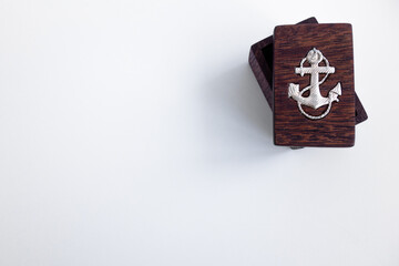 A mahogany wooden box with a metal anchor on a white isolate, an empty space for the text. Marine theme.