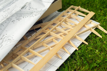 Assembling a wooden glider according to paper instructions on green grass. Modeling of airplanes.