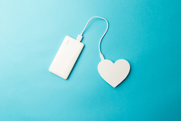 The power bank is connected to the heart on blue background. The concept of a healthy lifestyle....