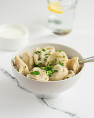 Boiled dumplings sprinkled with fresh herbs. Plate with dumplings on a light table