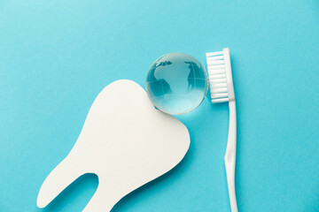 The concept of the International Day of the Dentist. White toothbrush, paper tooth and glass globe on a blue background. Top view. Flat lay. Close-up. Copy space