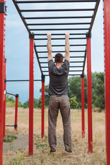 Strong young man hanging on a crossbar on the street in summer