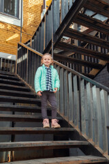 Little caucasian blonde girl in a fashionable outerwear stands on staircase