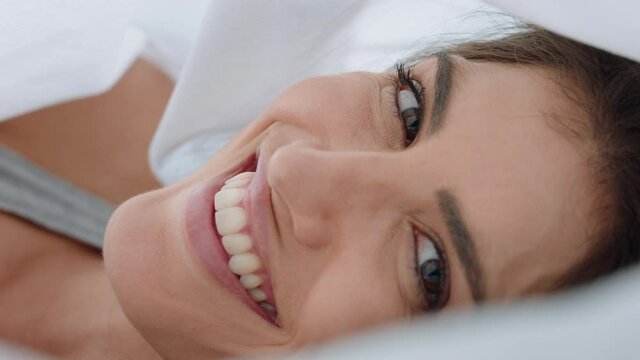 beautiful young woman playfully hiding under sheets lying in bed peeking through blankets smiling enjoying flirting having fun in morning 4k