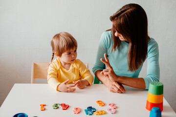 A young woman explains the numbers on her fingers to her little daughter. Teaching a child numbers concept