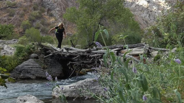 A hiker crosses a mountain river on an old bridge.