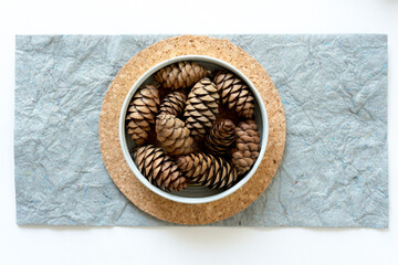 pine cones in a metal container on a cork and gray paper background