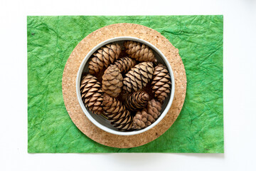 pine cones in a metal container on cork and green paper