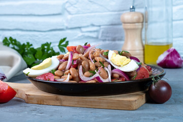 Turkish salad with white beans and tomatoes and red onions in a plate on a gray background.