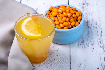 Sea buckthorn and lemon drink, bowl with sea buckthorn berries, wooden white background.