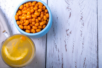 Sea buckthorn and lemon drink, bowl with sea buckthorn berries, wooden white background. Top view
