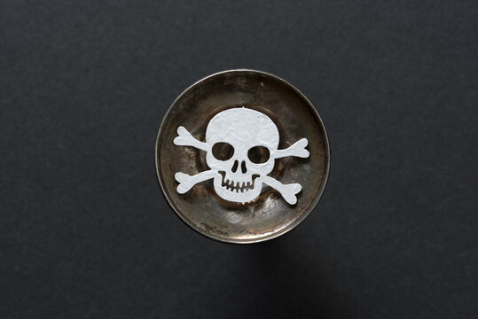 wooden skull and crossbones hand painted in white isolated on the bottom of a silver candle stick holder on black