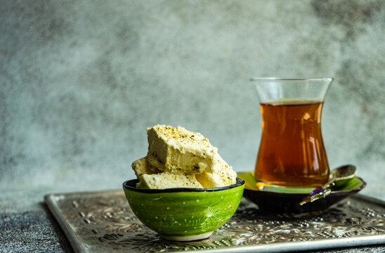 Cup of traditional Turkish sweet tea with a bowl of pistachio halva on a metal tray