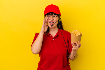 Young curvy caucasian woman fast food restaurant worker holding fries isolated on blue background shouting and holding palm near opened mouth.