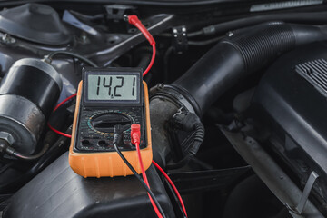 Voltage of the car's starter battery is measured by a multimeter. Voltage is about 14 volts when...