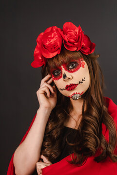 Portrait of a girl with Day of the Dead makeup covered with a red cape looking at the camera.