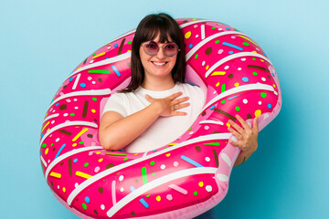 Young curvy caucasian woman with air mattress isolated on blue background laughs out loudly keeping hand on chest.