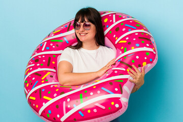 Young curvy caucasian woman with air mattress isolated on blue background looks aside smiling, cheerful and pleasant.