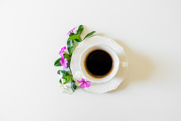 Black coffee cup, white flowers and blackberry tree leaves on white background. Flat lay, Top view. Spring concept.