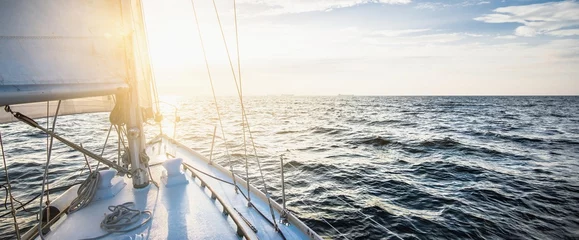 Foto op Plexiglas Yacht sailing in an open sea at sunset. Close-up view of the deck, mast and sails. Clear sky after the rain, glowing clouds, golden sunlight. Panoramic seascape © Aastels