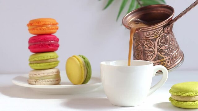 Coffee is poured into a cup on a table with colorful macaroons. Morning, tasty breakfast or pastries