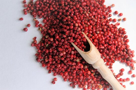 pink pepper on a white background with a wooden spoon