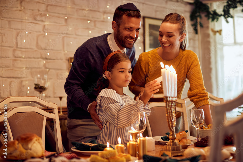 Wall mural happy jewish family lights menorah candles before meal at dining table during hanukkah.